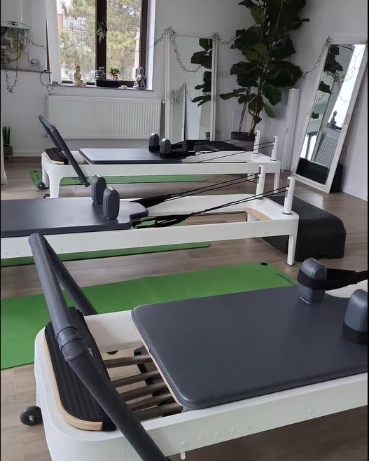 Sala Studio Pilates Deva: reformere albe pe saltele verzi, oglinzi și plante